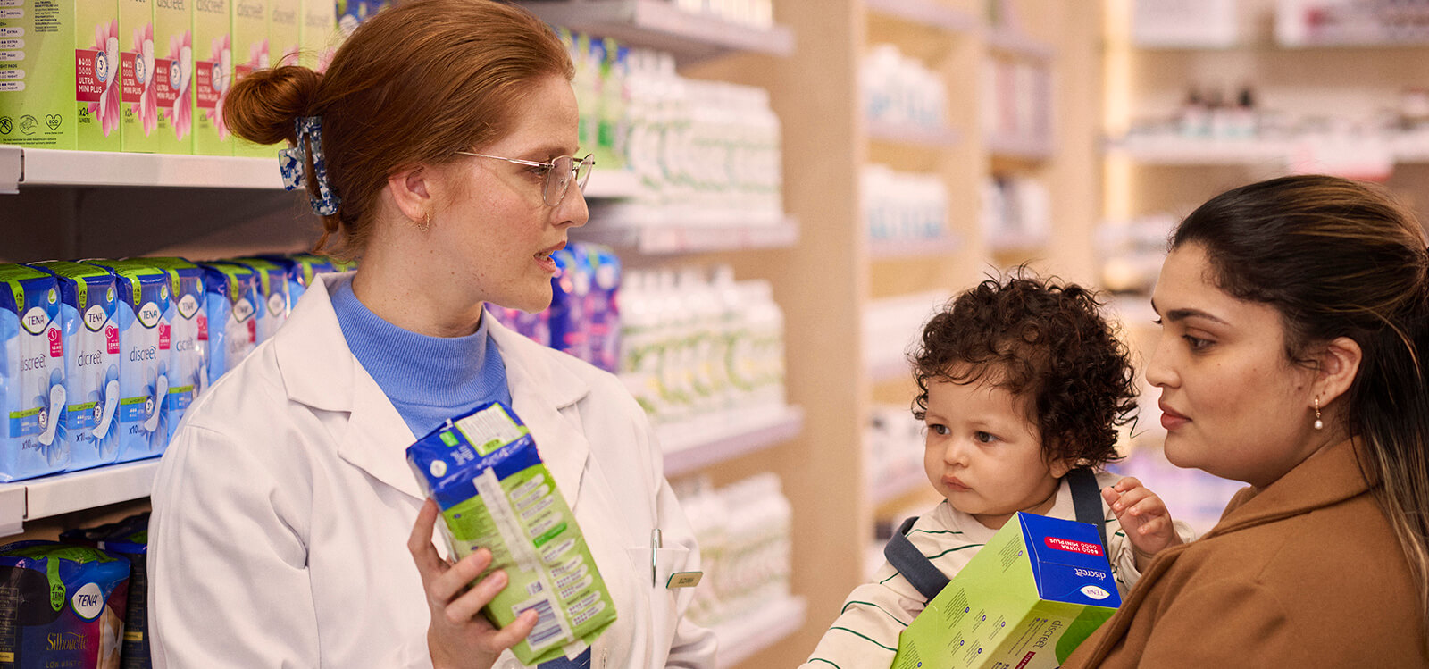 Pharmacist showing TENA product to Mother with small child
